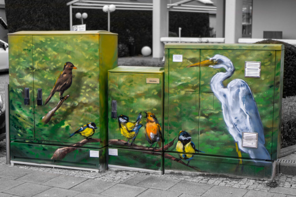 Bunte Straßengraffiti mit Vögeln auf Stromkästen vor Wohnhäusern.