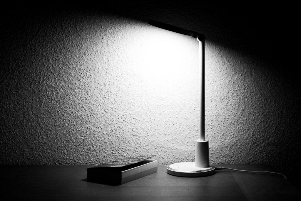 Minimalistische Tischlampe beleuchtet eine strukturierte Wand, daneben liegt ein geschlossenes Buch.