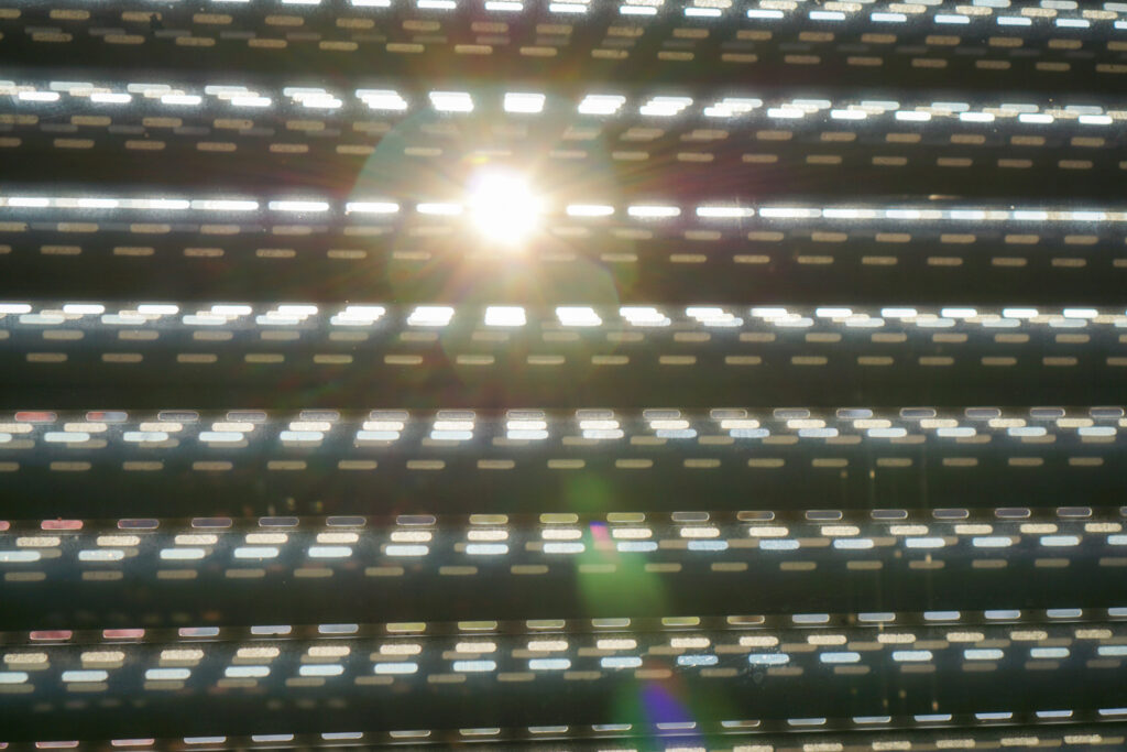 Sonnenlicht scheint durch die schmalen Schlitze eines heruntergelassenen Rollladens und erzeugt helle Lichtmuster sowie einen leichten Blendenfleck.