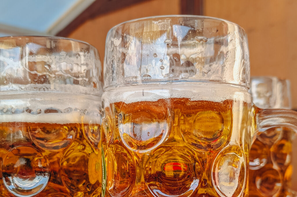 Mehrere Bierkruege mit goldgelbem Bier und Schaum stehen dicht nebeneinander, mit Lichtreflexen im Glas