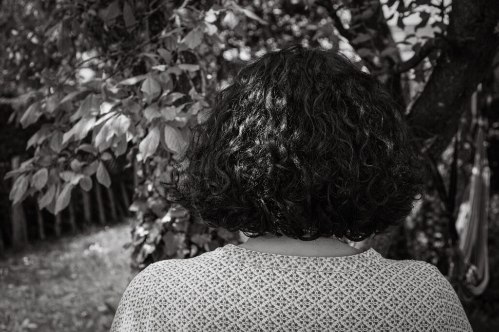 Eine Person mit lockigem Haar steht mit dem Rücken zur Kamera im Garten.
