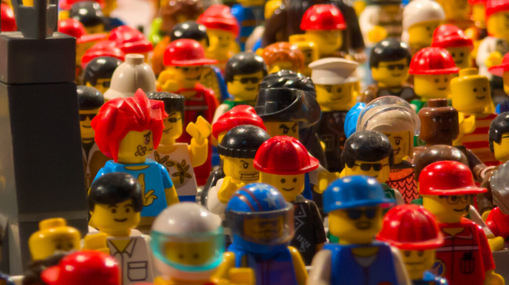 Dicht gedrängte LEGO-Minifiguren mit bunten Helmen und Frisuren in einer Menschenmenge.