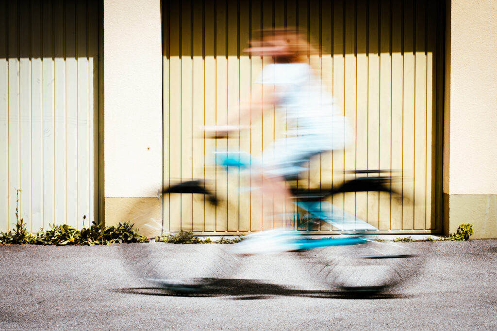 Unscharfe Person auf Fahrrad vor Garagentoren, Bewegungsunschärfe betont Geschwindigkeit.