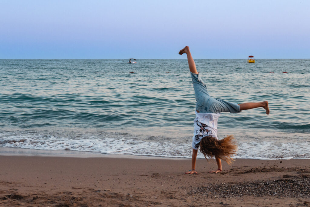 Eine Person macht einen Radschlag am Strand vor dem Meer.