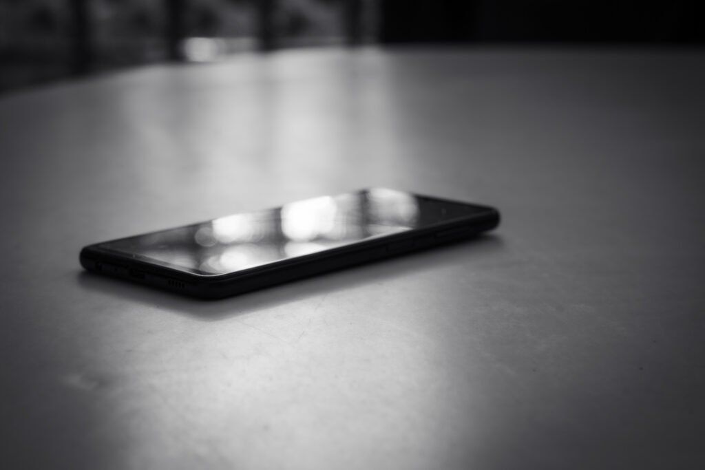 Schwarz-weisses Smartphone auf glatter Fläche mit Lichtreflexen auf dem Bildschirm.