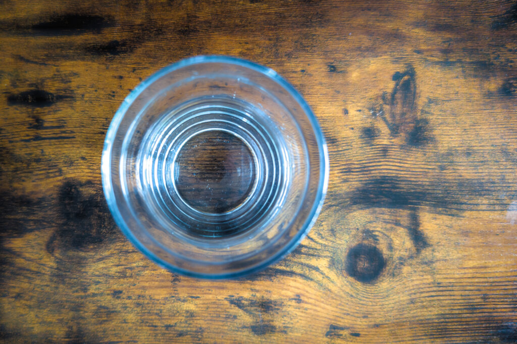 Glas mit Wasser auf einem rustikalen Holztisch, aus der Vogelperspektive fotografiert.