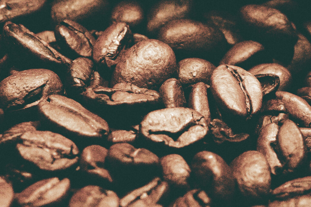 Makroaufnahme gerösteter Kaffeebohnen mit brauner Oberfläche, feinen Rissen und sichtbaren Strukturen vor dunklem Hintergrund.