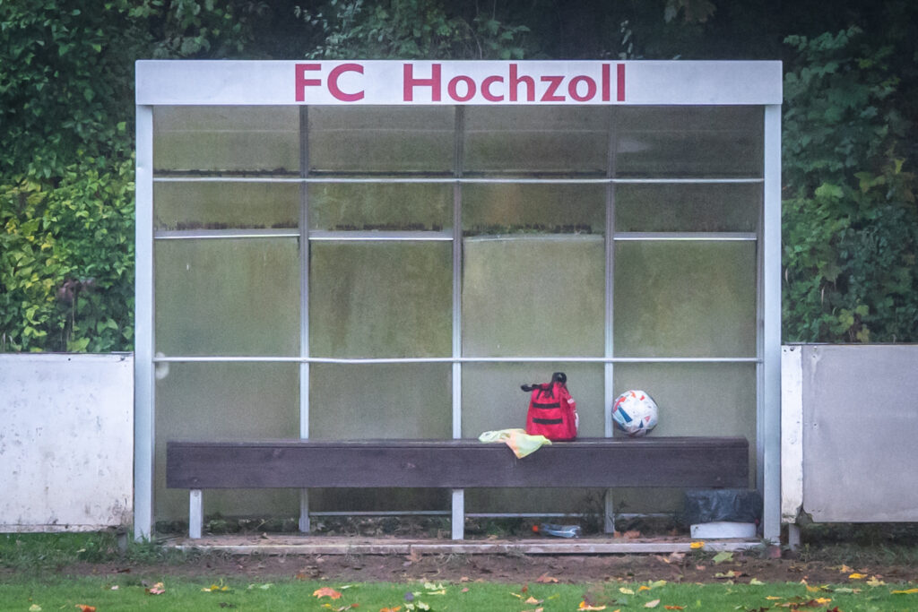 Mannschaftsunterstand des FC Hochzoll mit Fussball, rotem Rucksack und Trainingsleibchen auf der Bank.