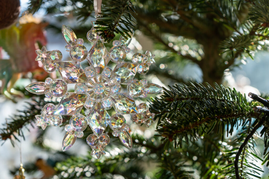 Kristall-Schneeflockenanhaenger glitzert an gruenen Tannenzweigen eines Weihnachtsbaums