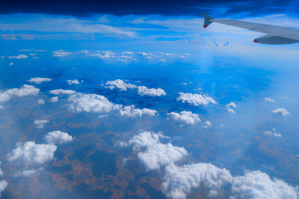 Blick aus dem Flugzeugfenster auf Tragfläche, Wolkenmeer und blauen Himmel über weiter Landschaft.
